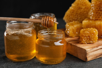 Honey dripping from dipper into jar on grey table