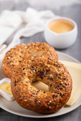 fresh bagels with butter and cheese on plate and cup of coffee on ceramic background