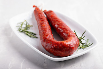 smoked sausage with rosemary on white dish on ceramic background