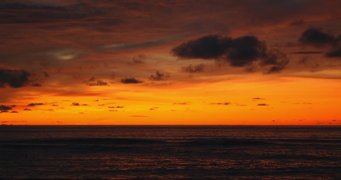Tropical beach. Dark orange clouds day to night sky reflected in big waves crushing coast. Beautiful dramatic sunset sky. Red purple orange blue pink sunset cloud background. Ocean surfer lifestyle.