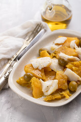 cod fish with sweet potato and olives on dish on ceramic background