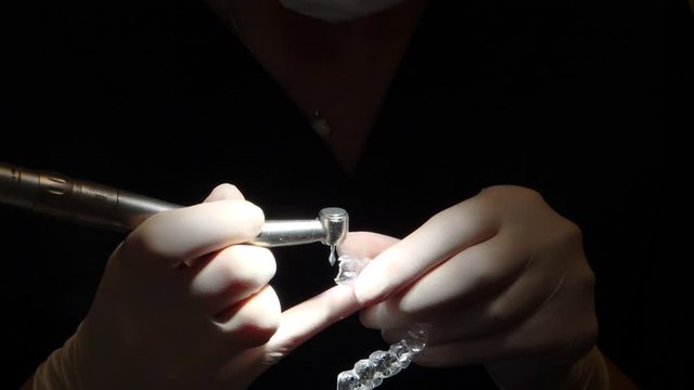 close-up view of orthodontist hands, working on an invisalign aligner, in dark setting with focus light