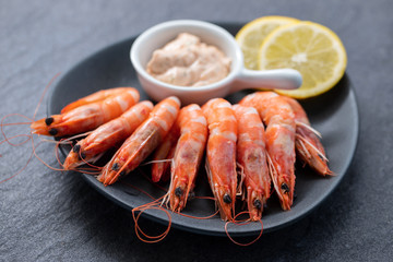 boiled shrimps with lemon and sauce on white dish on ceramic background