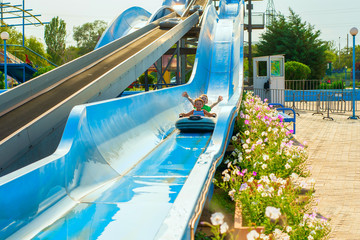 Children on a water slide, two boys descend on an inflatable boat in an amusement park.