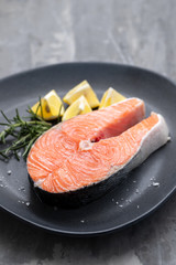 raw salmon with rosemary and lemon on dark plate