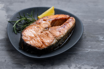 fried salmon with lemon and rosemary on dark dish on ceramic background