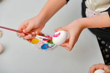 Obraz na płótnie Canvas Children paint eggs for Easter, paints draw patterns on a white egg.