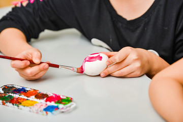 Children paint eggs for Easter, paints draw patterns on a white egg.