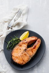 fried salmon with lemon and rosemary on dark dish on ceramic background