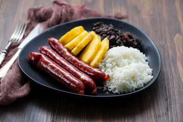 sausages with rice, black beans, and pineapple on dark dish