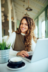Attractive young curly brunette enjoying her coffee and working on laptop	