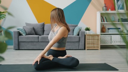 Beautiful young woman is doing yoga relaxing in lotus asana with hands in namaste gesture meditating at home. Relaxation, modern lifestyle and apartment concept.