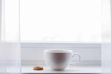 white cup with tea stands on the windowsill on the window