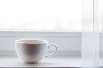 white cup with tea stands on the windowsill on the window