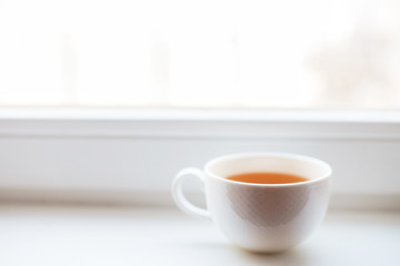 white cup with tea stands on the windowsill on the window