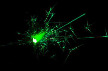 Sparkler in green and white light on a black background