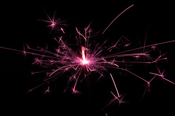 Sparkler in pink and white light on a black background.