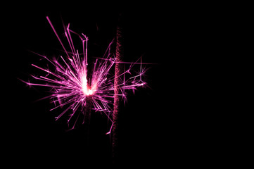 Sparkler in pink and white light on a black background.