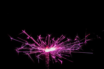 Sparkler in pink and white light on a black background.