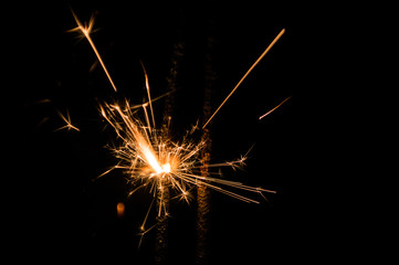Fototapeta premium Sparkler in yellow and orange light on a black background.