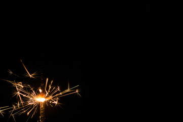 Fototapeta premium Sparkler in yellow and orange light on a black background.