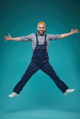 Vertical studio full shot of cheerful young adult guy in workwear having fun jumping, blue...
