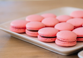 Beautiful pink macaroons with chocolate ganache on a white square plate stand on a wooden table