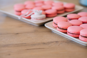 Beautiful pink macaroons with chocolate ganache on a white square plate stand on a wooden table