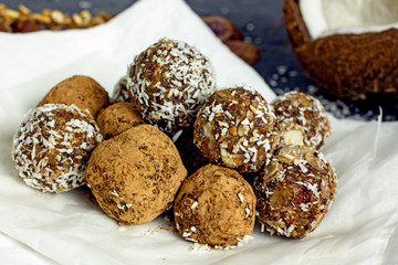 Raw food balls.Handmade vegan sweets made from almonds, walnuts, dates, raisins, coconut and cocoa. Raw food candies in coconut and cocoa close-up on white paper on a dark table laid out in rows. 