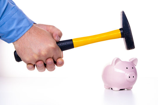 Male hand smashes a pink pig piggy bank with a hammer on a white background. The concept of savings and savings, financial management