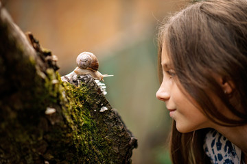 Joyful meeting of a little girl and a snail. Summer photo in the rain.