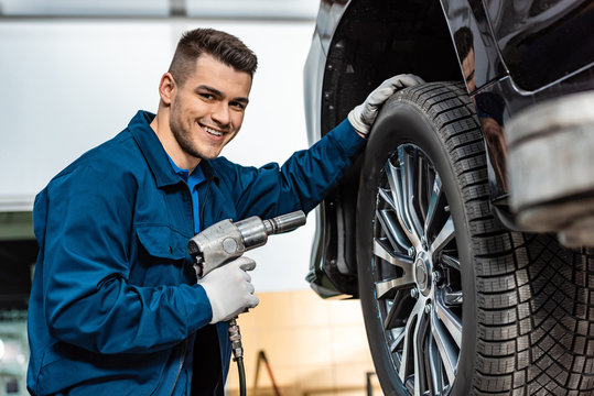 cheerful mechanic looking at camera while holding pneumatic wrench - Powered by Adobe