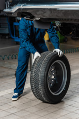 Obraz na płótnie Canvas cropped view of mechanic with wheel near raised car in workshop