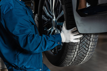 cropped view of mechanic installing new tire on car - obrazy, fototapety, plakaty