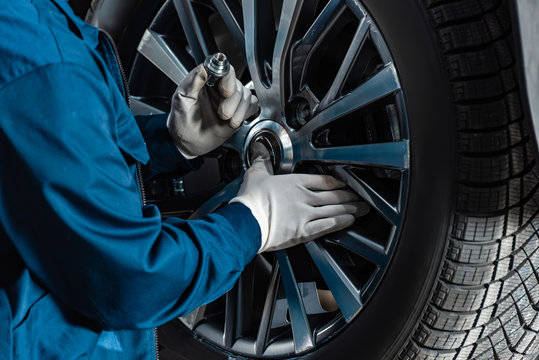 cropped view of mechanic fixing wheel on car in workshop