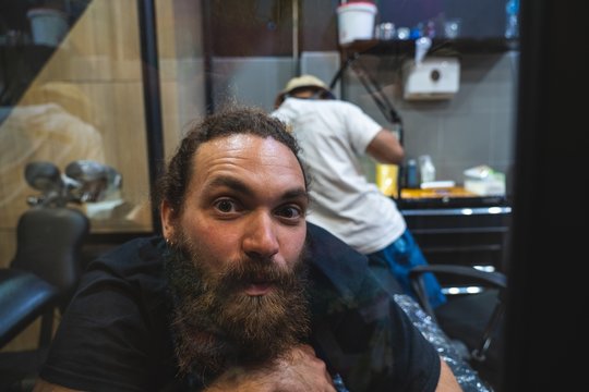 Bearded man with a surprise and emotional expression while a tattoo artist make him a tattoo with a bamboo stick in Bangkok (Thailand)