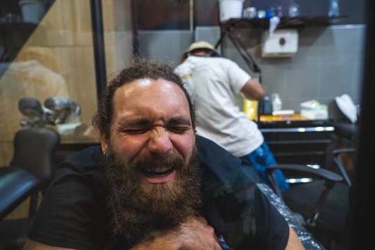 Bearded man suffering pain while a tattoo artist make him a tattoo with a bamboo stick in Bangkok (Thailand)