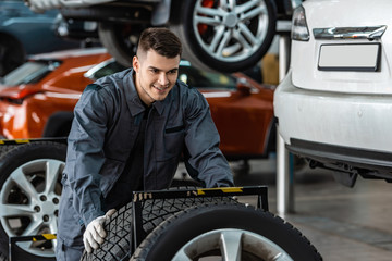 handsome, smiling mechanic holding new tire in workshop