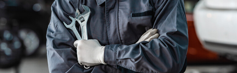 cropped view of mechanic holding wrenches while standing with crossed arms