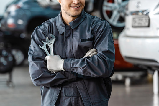 cropped view of smiling mechanic standing with crossed arms and holding wrenches