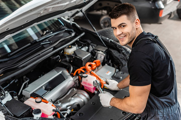 handsome mechanic inspecting car engine compartment and smiling at camera