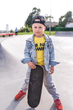 Little boy 3-5 years old, learning to ride skateboard, autumn day, casual warm clothes. Denim with a baseball cap. Driving lessons, first experience, outdoor sports. Posing in hand skate.