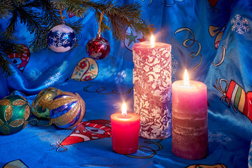 burning candles under a Christmas tree with colored balls on a blue tablecloth