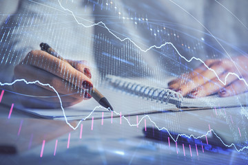 Double exposure of woman's hands making notes with forex graph hologram. Concept stock market analysis.