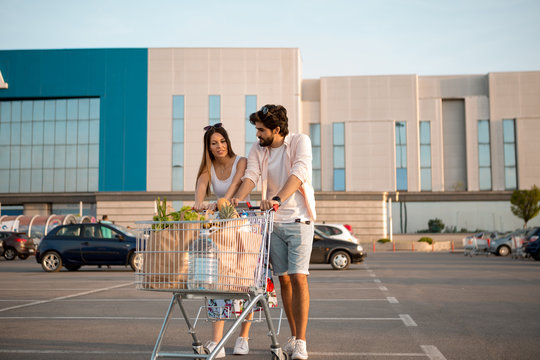 Young married couple talking about home budget after shopping in a big market. They are in front of the shopping mall and are pushing big carts full of groceries. Shopping. Food.