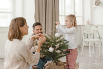 Cute baby girl with her parents play in a spacious bright minimalistic kitchen.