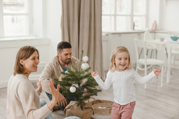 Cute baby girl with her parents play in a spacious bright minimalistic kitchen.