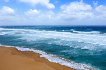 Aerial view turquoise waves push ashore on yellow sand beach, land meets sea. Great Ocean Road, Australia.
