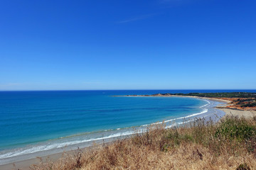 Fototapeta na wymiar Summer view of pure blue crescent shaped beach coastline, Great Ocean Road, Victoria, Australia.