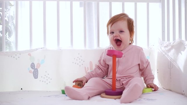 cute little baby girl playing with colorful wooden stacking rings in the crib